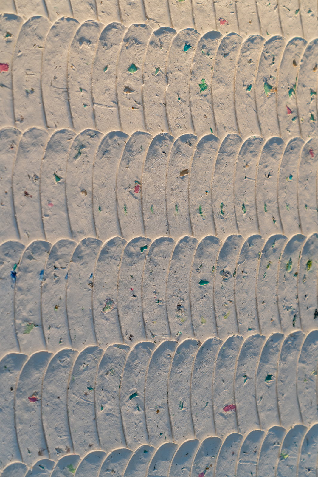 The white impasto close up: arched ribbed strips set in rows, flecked with green, pink and blue fragments.