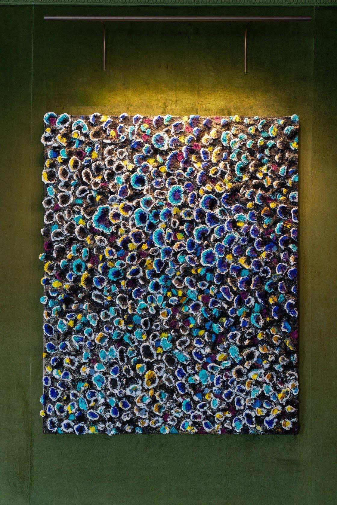 The rosette panel close up: hundreds of small raised flowers in blue, turquoise, yellow and white over a dark ground.