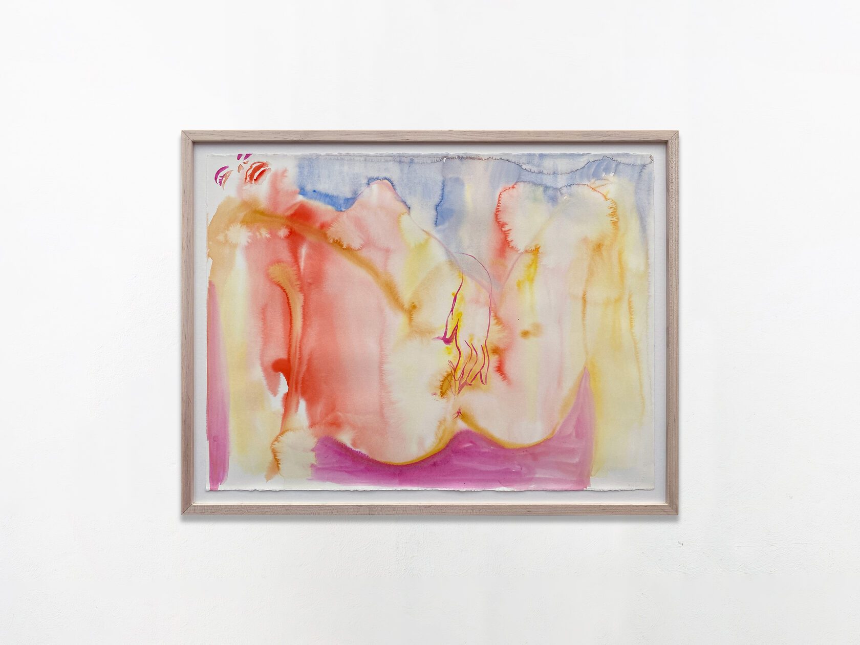 A framed work on paper hung alone on a white wall, washed in pink, red, yellow and blue, with a body suggested along the lower edge.