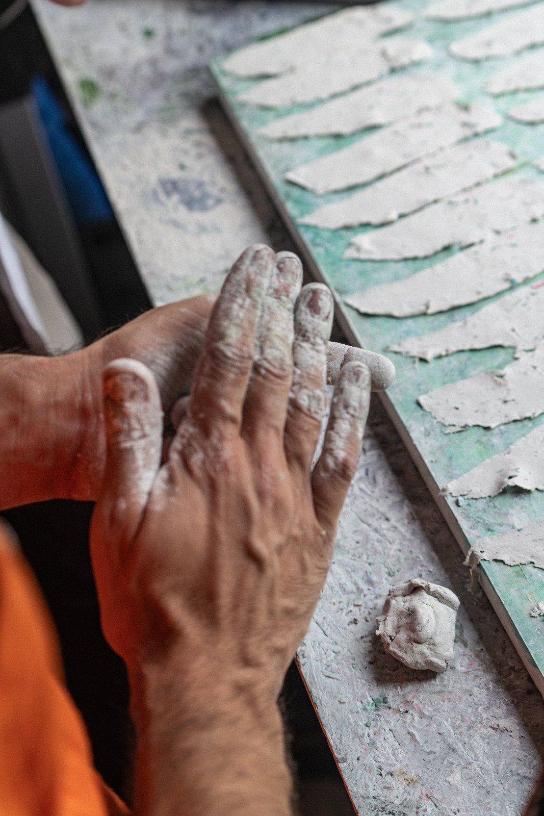 The artist’s hands at a work surface, slices of white clay laid out in a row beside a tray.