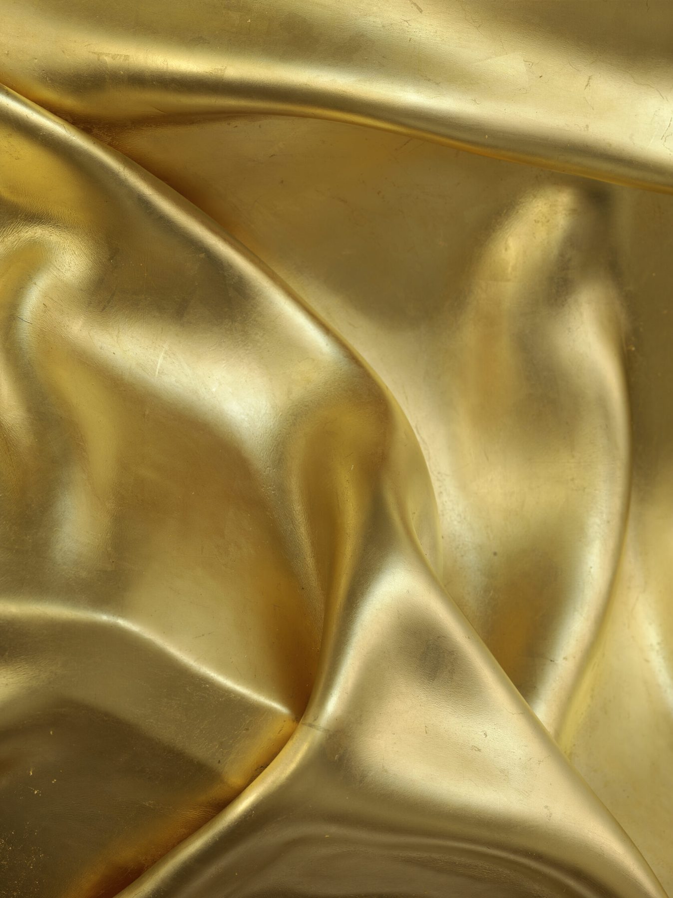 A gold surface pressed into deep soft folds that run off every edge of the frame, lit so the creases turn from bright to shadow.